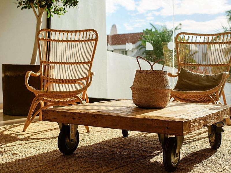 Hell beleuchteter Raum mit zwei Rattanstühlen und einem niedrigen Holztisch auf Rädern.