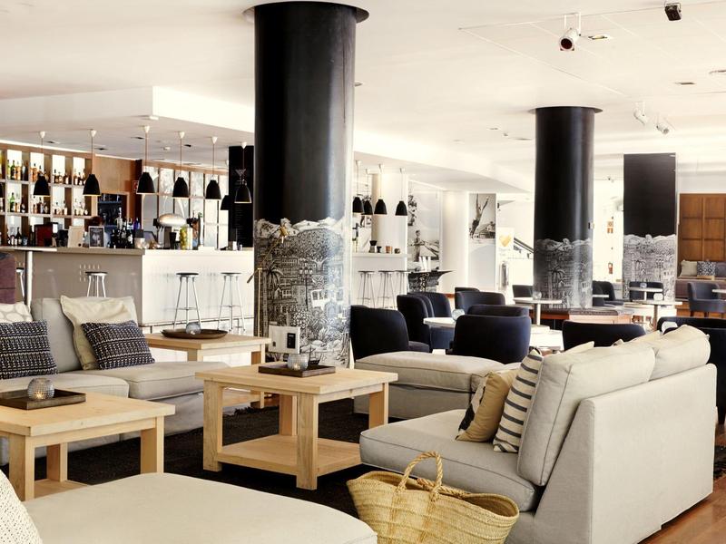 Heller, moderner Lounge-Bereich mit bequemen Sofas, Holztischen und schwarzem Säulendesign.