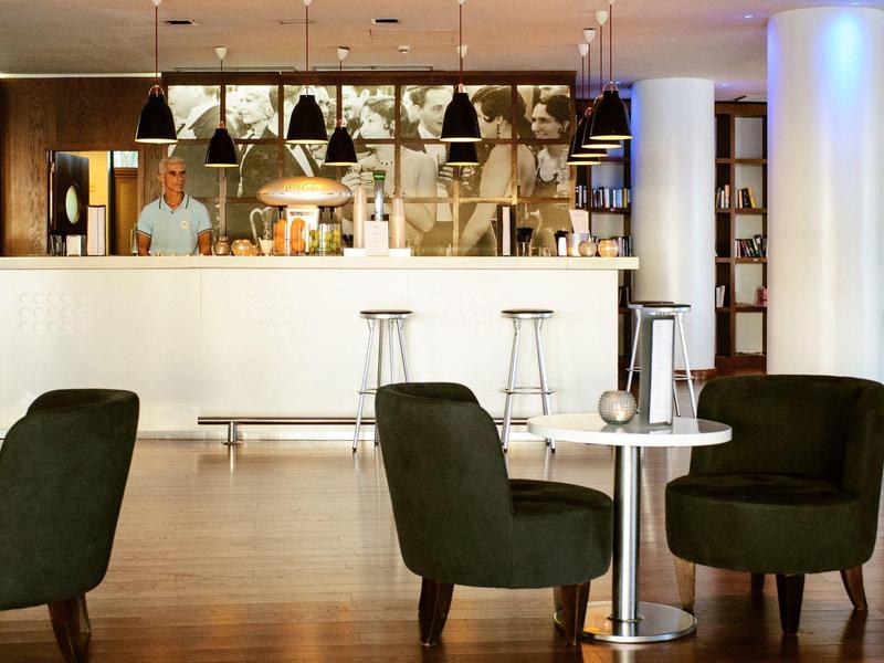 Moderne Bar mit weißem Tresen, schwarzen Stühlen und Holzfußboden, freundliche Beleuchtung.