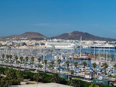 Harbor with many boats in front of a coastal town and two hills in the background under clear sky.