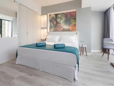 Chambre d'hôtel moderne avec lit double, serviettes bleues, et grande fenêtre lumineuse.