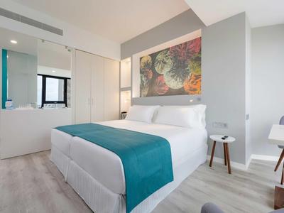 Chambre d'hôtel moderne avec lit double, décor coloré et sol clair.