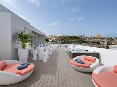 Terrasse d'hôtel avec fauteuils ronds, jacuzzi et vue sur la ville sous un ciel dégagé.
