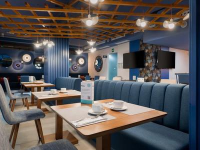 Intérieur d'un restaurant moderne avec tables en bois, chaises bleues et lumière chaleureuse.