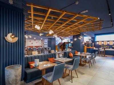 Modern hotel restaurant area with blue seating, wooden tables, and decorative wooden ceiling.