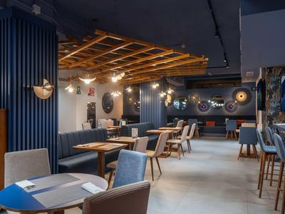 Restaurant moderne avec tables en bois, chaises grises et éclairage chaleureux.