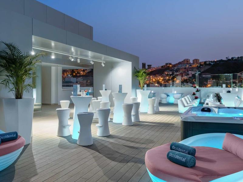 Terrasse d'hôtel moderne avec mobilier blanc et vue sur la ville au crépuscule.