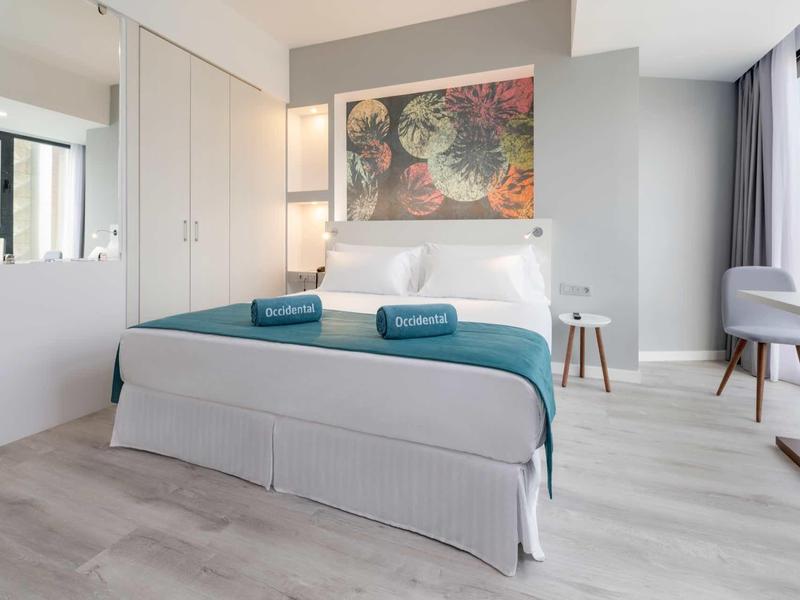 Chambre d'hôtel moderne avec lit double, serviettes bleues, et grande fenêtre lumineuse.