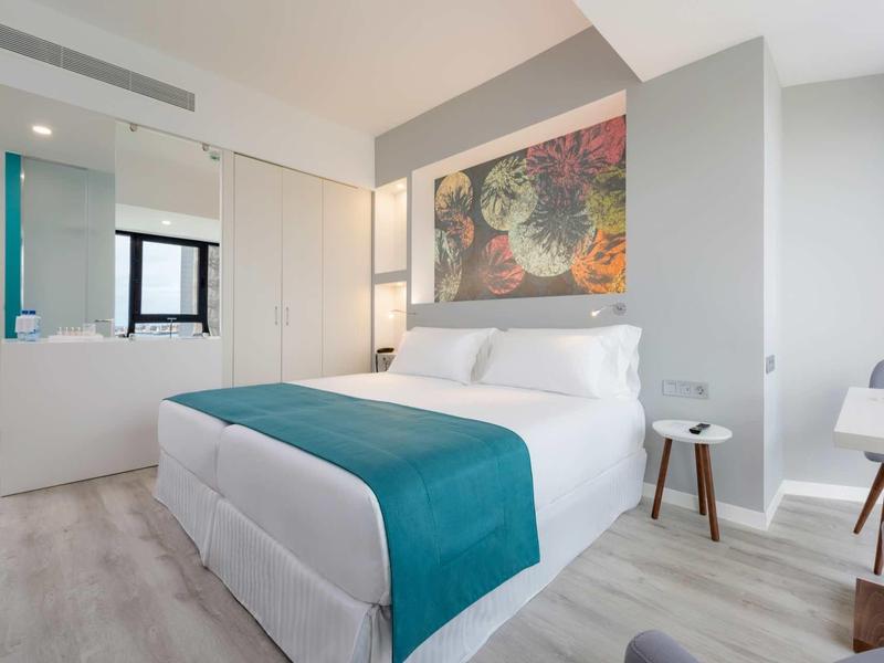 Chambre d'hôtel moderne avec lit double, décor coloré et sol clair.