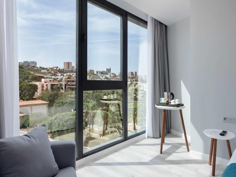 Salon lumineux avec grandes fenêtres donnant sur un paysage urbain et mobilier moderne.