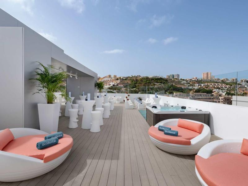 Terrasse d'hôtel avec fauteuils ronds, jacuzzi et vue sur la ville sous un ciel dégagé.