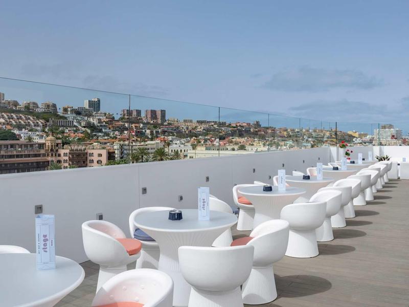 Terrasse moderne avec tables blanches et chaises design surplombant la ville.