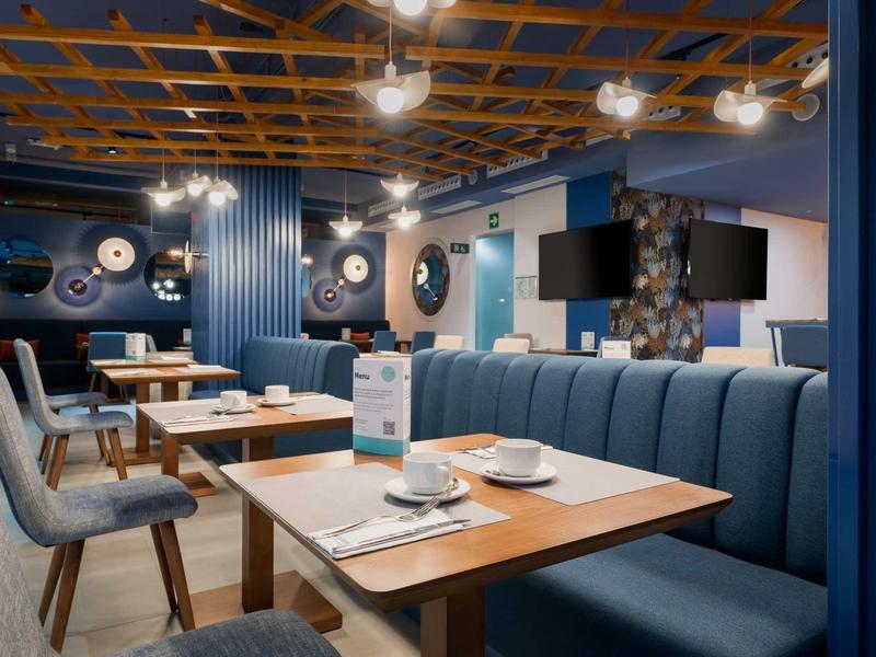 Intérieur d'un restaurant moderne avec tables en bois, chaises bleues et lumière chaleureuse.