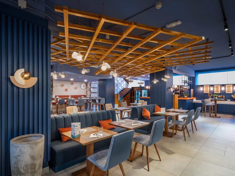 Restaurant moderne avec sièges bleus, tables en bois et éclairage chaleureux.