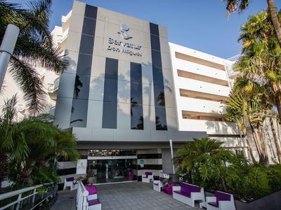 Nowoczesny hotel ze szklaną fasadą i palmami, białe i fioletowe meble na zewnątrz przy wejściu