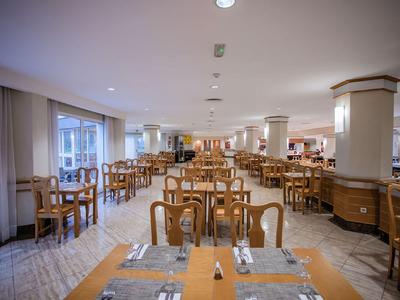 Duża, jasna jadalnia z wieloma drewnianymi stołami i krzesłami w hotelu.