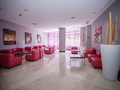 Jasna strefa wypoczynkowa hotelu z czerwonymi skórzanymi fotelami, sztuką współczesną i dużymi oknami.