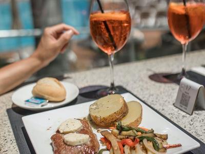 Talerz z stekiem, ziemniakami i warzywami obok Aperol Spritz na stole na zewnątrz.