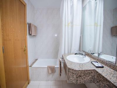 Czysta łazienka z marmurową umywalką, białą zasłoną prysznicową i drewnianymi elementami.