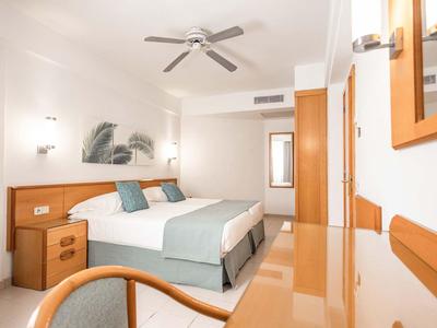 Jasny pokój hotelowy z podwójnym łóżkiem, wentylatorem sufitowym i nowoczesnym wyposażeniem.