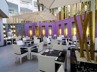 Nowoczesna, stylowa część restauracyjna hotelu z białymi krzesłami i czarnymi stołami pod dużym parasolem.