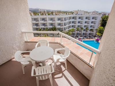 Balkon mit rundem weißen Tisch und vier Stühlen, Blick auf Swimmingpool und Hotelgebäude im Hintergrund.