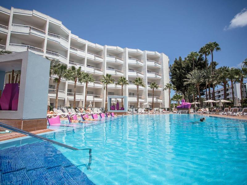 Duży hotelowy basen z leżakami i palmami pod niebieskim niebem.