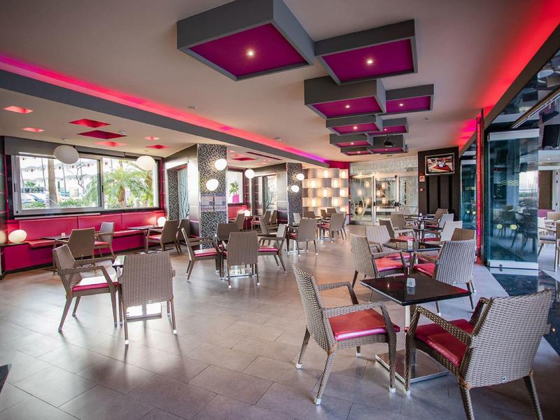 Nowoczesna restauracja z szarymi krzesłami, czerwonymi akcentami i dużymi oknami z widokiem na drzewa.