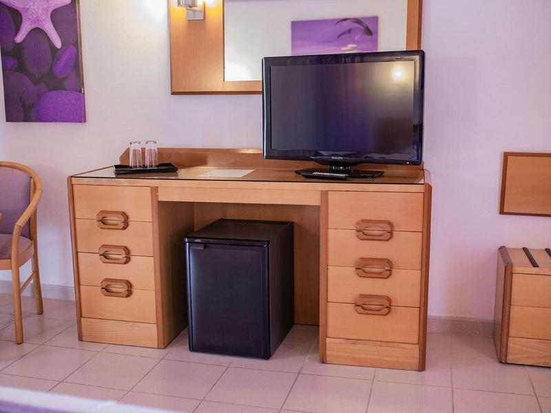 Biurko z małą lodówką, telewizorem i lustrem w pokoju hotelowym.