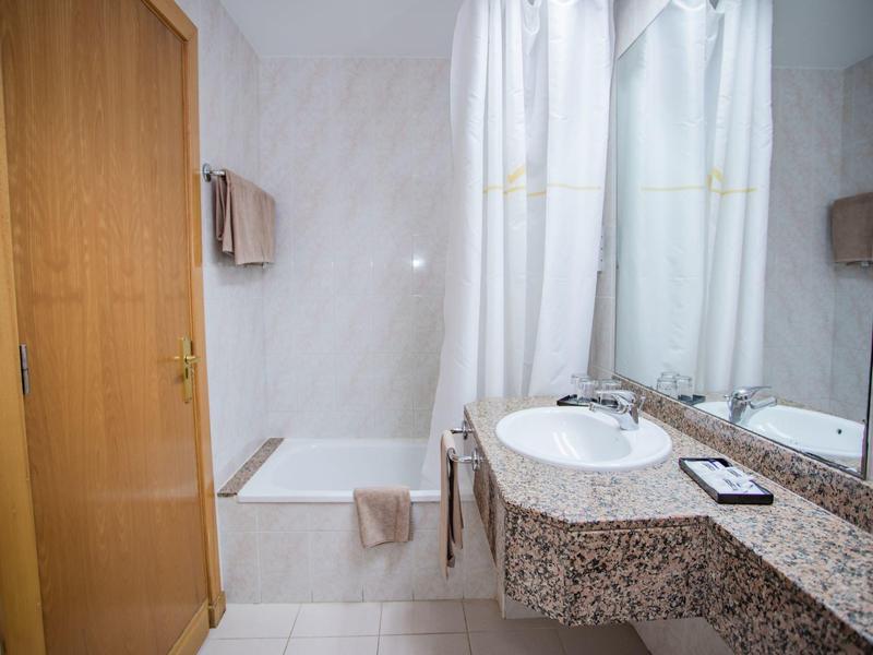 Czysta łazienka z marmurową umywalką, białą zasłoną prysznicową i drewnianymi elementami.