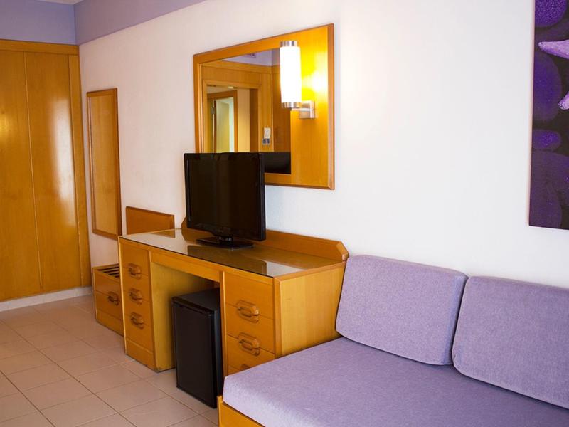 Pokój hotelowy z fioletową sofą, telewizorem na drewnianym stole i szafą na ścianie.