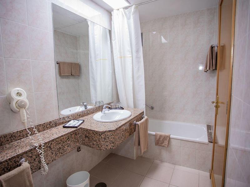 Nowoczesna łazienka hotelowa z dużym lustrem, umywalką, wanną i suszarką do włosów.