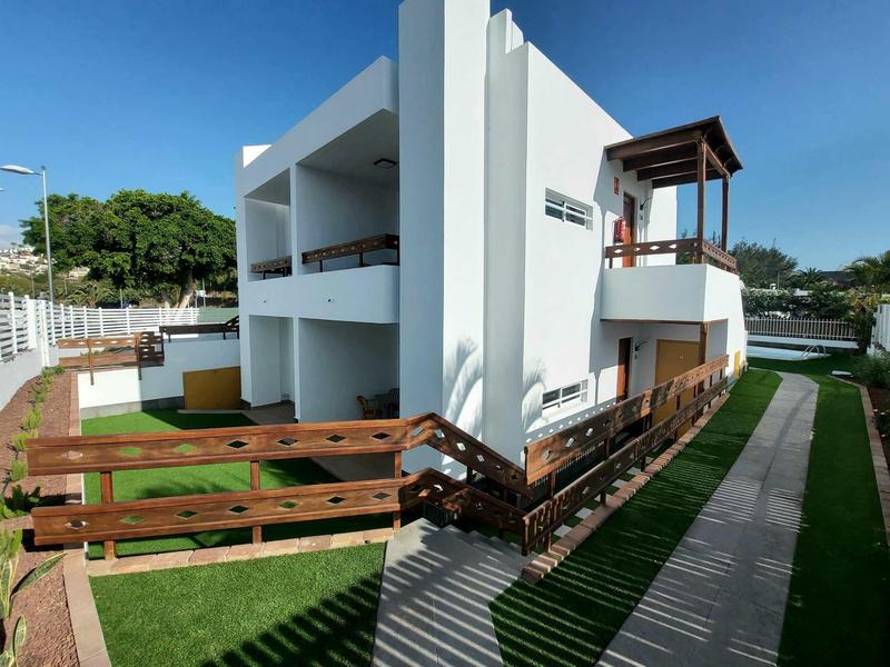 Moderní bílý dvoupodlažní dům s balkony, dřevěnými zábradlími a upraveným trávníkem.