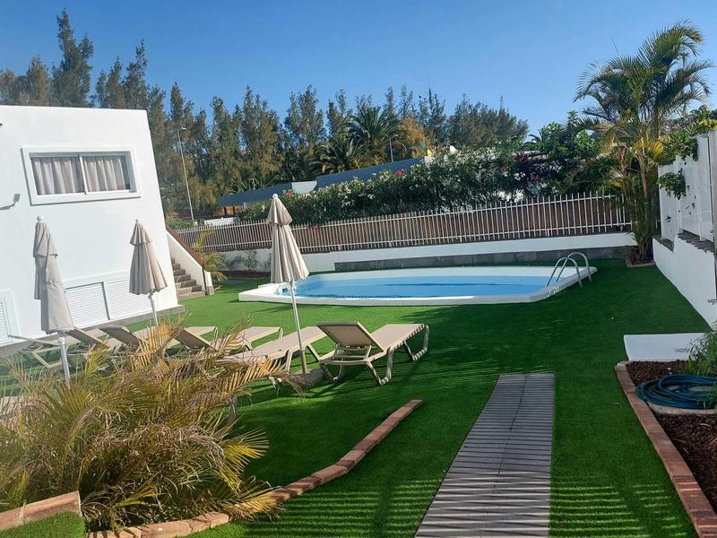 Moderní zahrada s bazénem, lehátky a slunečníky vedle bílé budovy.