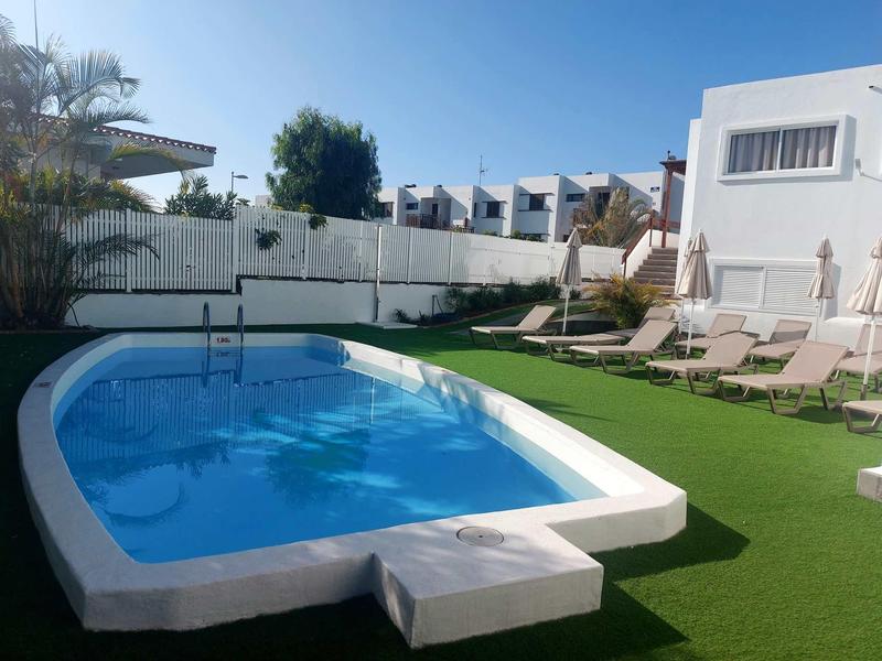 Malý bazén s lehátky na zelené trávě v hotelové zahradě pod jasnou oblohou.