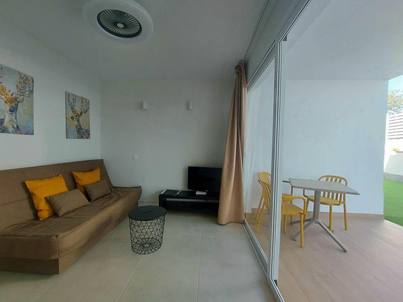 Moderně zařízený obývací pokoj s hnědým gaučem, TV a světlým balkonem s jídelním stolem.