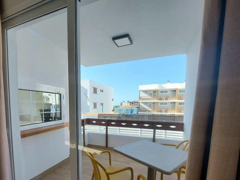 Balkon se stolem a židlemi, výhled na sousední budovy za jasné oblohy.