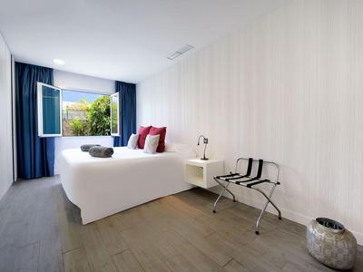 Moderne, lichte slaapkamer met wit bed, rode kussens en open raam met uitzicht op groen.