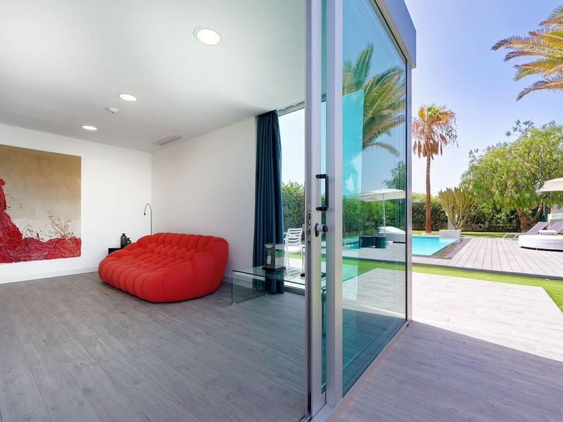 Moderní obytný prostor s červenou pohovkou a výhledem na terasu s bazénem a zahradou.