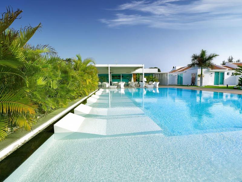 Moderní hotelový bazén s lehátky, palmami a jasně modrou oblohou