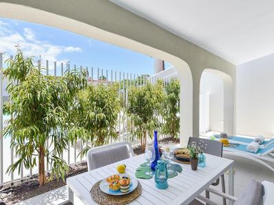 Overdekt terras met eettafel en ligstoelen naast een zwembad en groene planten.