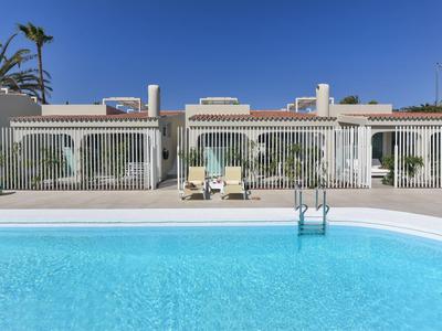 Piscina limpida davanti a case vacanze di un piano sotto un cielo soleggiato.
