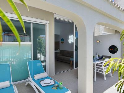 Hotelterras met twee blauwe ligstoelen voor een open deur naar een kamer.