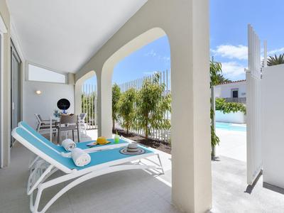 Lichtblauwe ligstoelen op balkon met uitzicht op zwembad en groene planten op een zonnige dag.