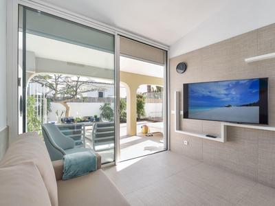 Moderne woonkamer met bank, aan de muur gemonteerde tv en toegang tot terras met tuinmeubilair.