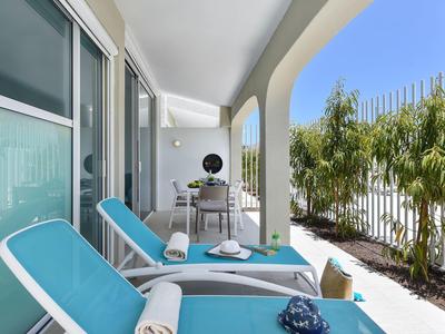 Balkon met blauwe ligstoelen, tafel en uitzicht op groene planten in een hotel.