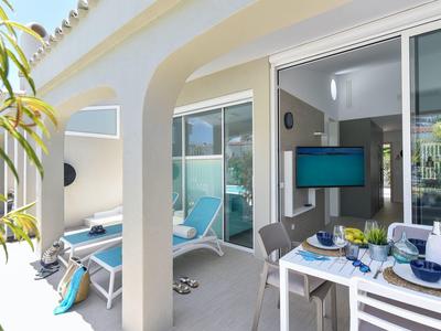 Lichte balkon met eettafel, stoelen en uitzicht op een woonkamer met tv in een vakantiewoning.