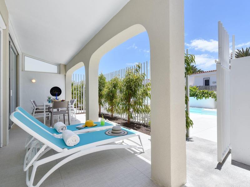 Lichtblauwe ligstoelen op balkon met uitzicht op zwembad en groene planten op een zonnige dag.
