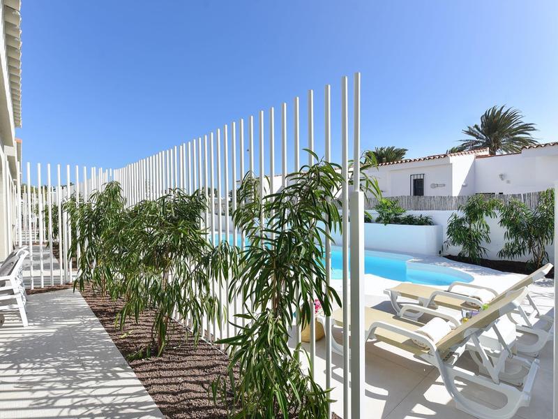 Moderne buitenruimte met zwembad, ligstoelen en witte gebouwen onder een heldere lucht.