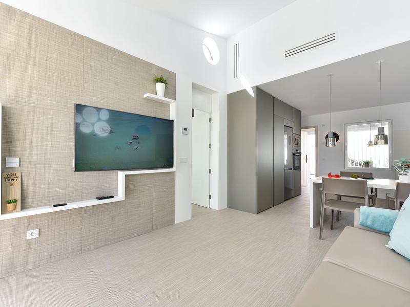 Lichte moderne woonkamer met wand-tv, bank en uitzicht op eetgedeelte en keuken.